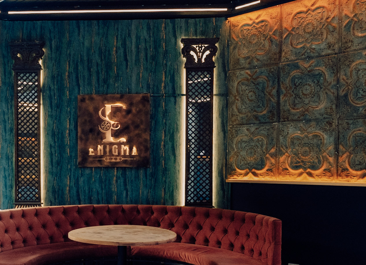 Interior del bar Enigma: pared teal, sofá de terciopelo carmesí y el letrero de cobre
