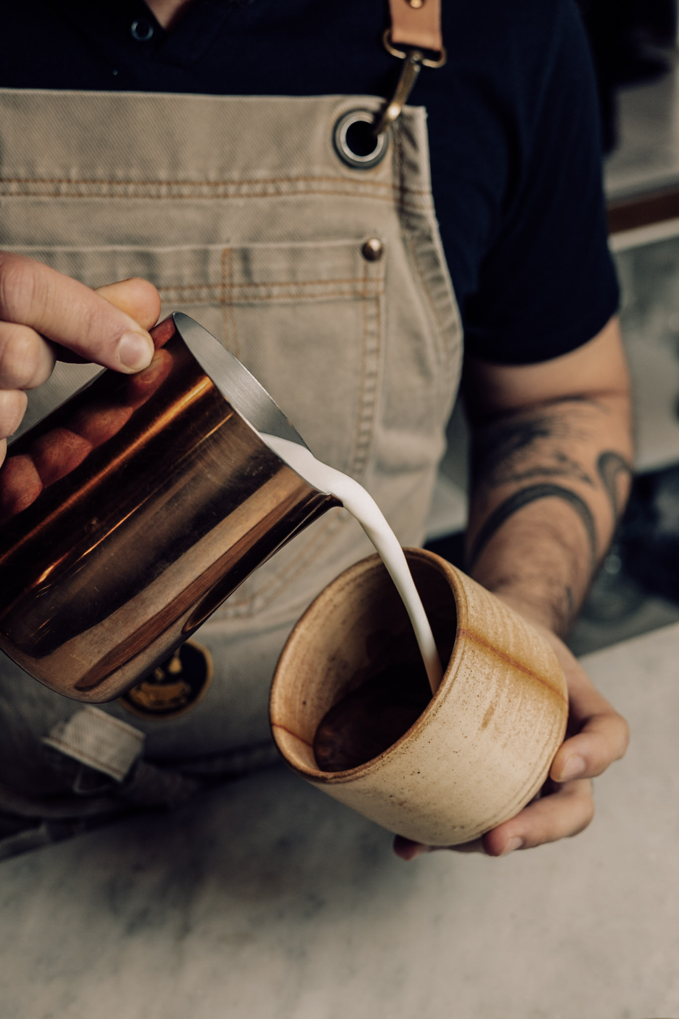 Barista vertiendo leche texturizada en una taza de greda