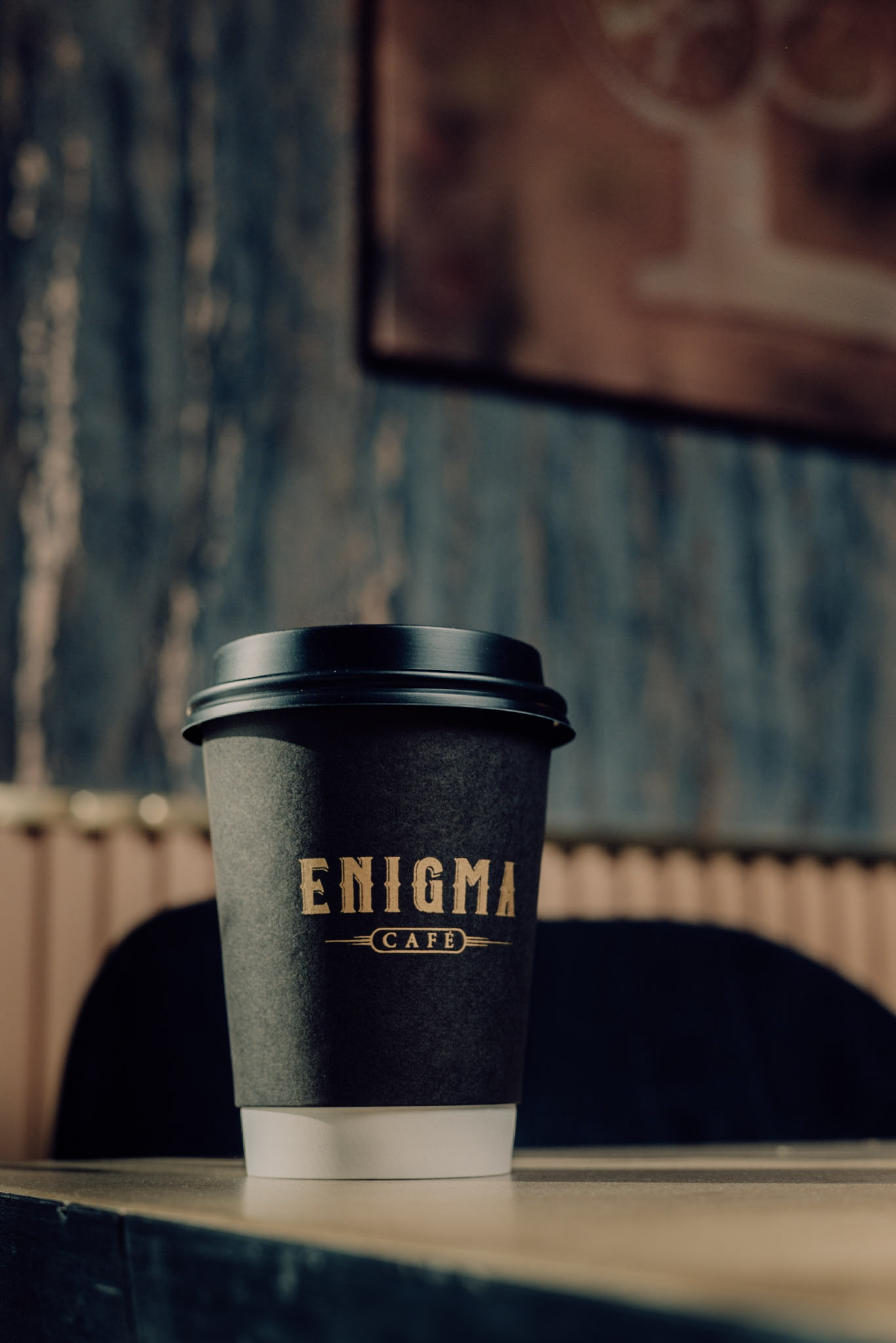 Vaso negro de Enigma Café con el logotipo dorado