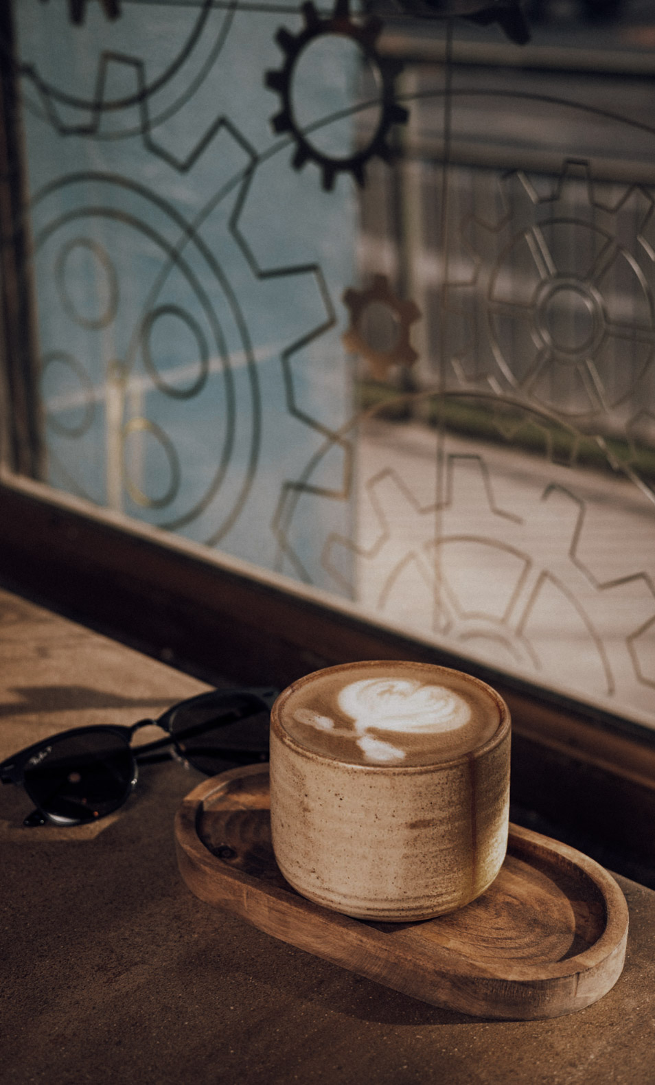 Latte sobre bandeja de madera junto a un vidrio con engranajes grabados